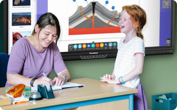 student and teacher laughing in the classroom with an interactive display in the background.