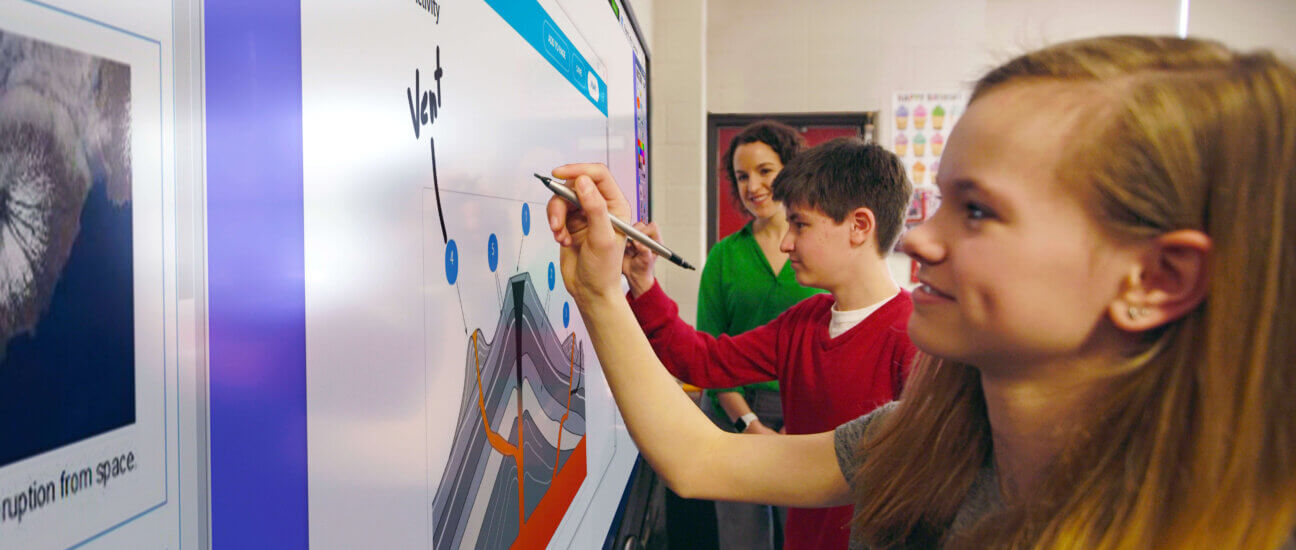 Two students draw on a digital presentation displayed on an interactive display