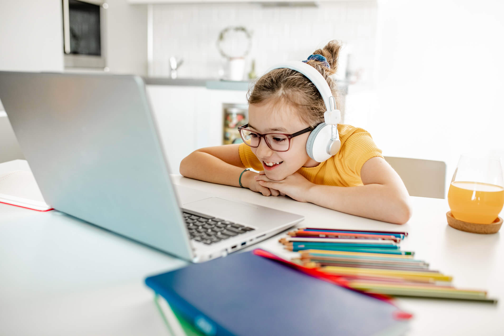 Schoolgirl with headphones and laptop sitting at a desk at home, watching an educational video.