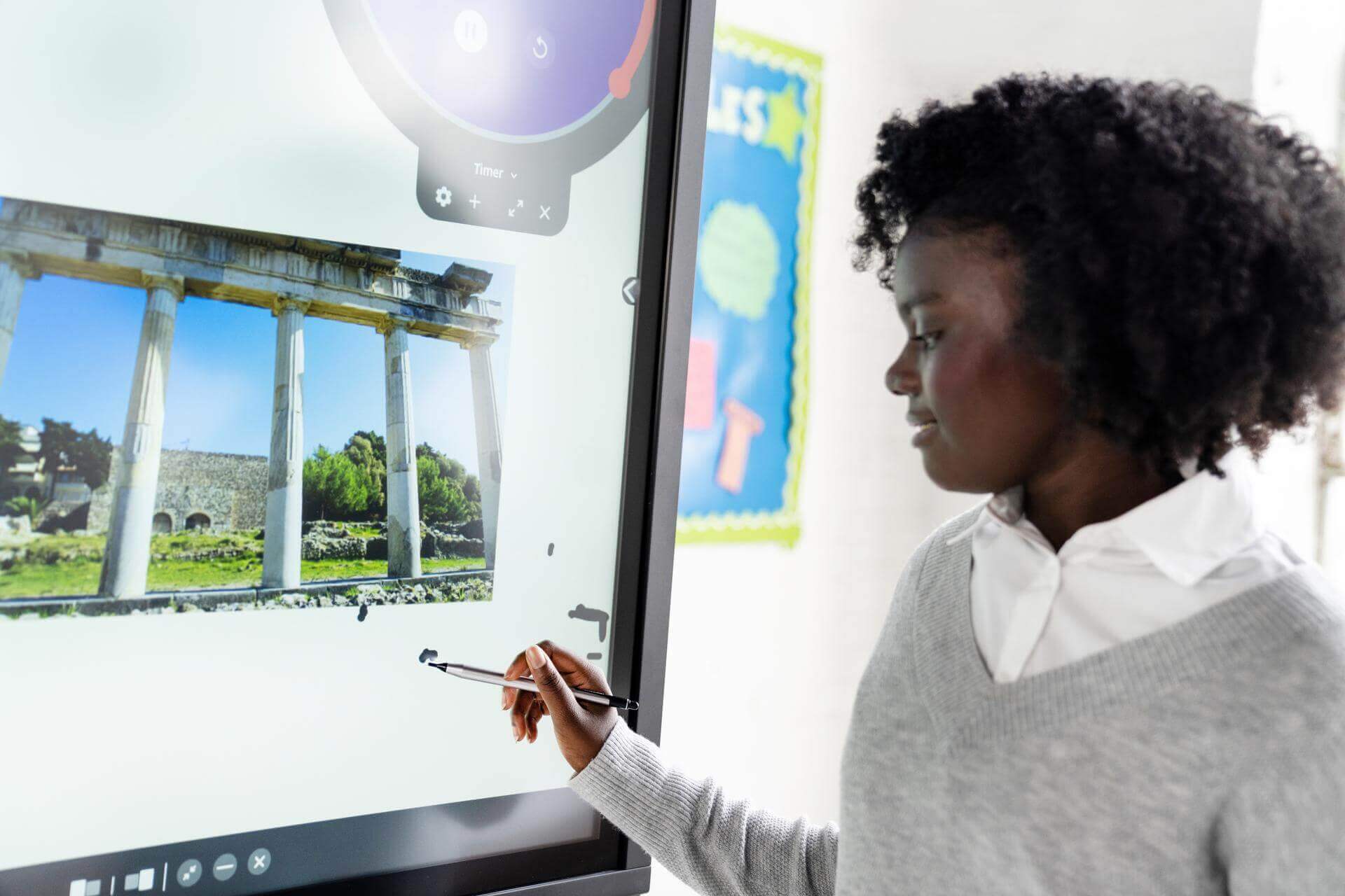 Un enfant dessine sur un écran numérique interactif.