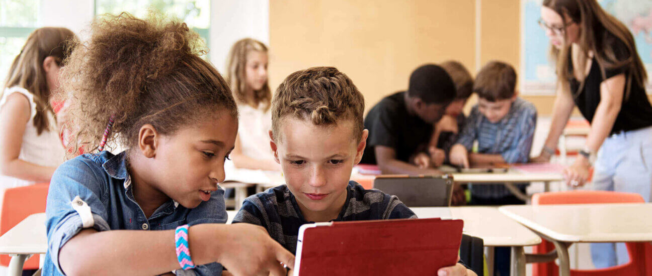 Two primary-age school students work together on a digital tablet.