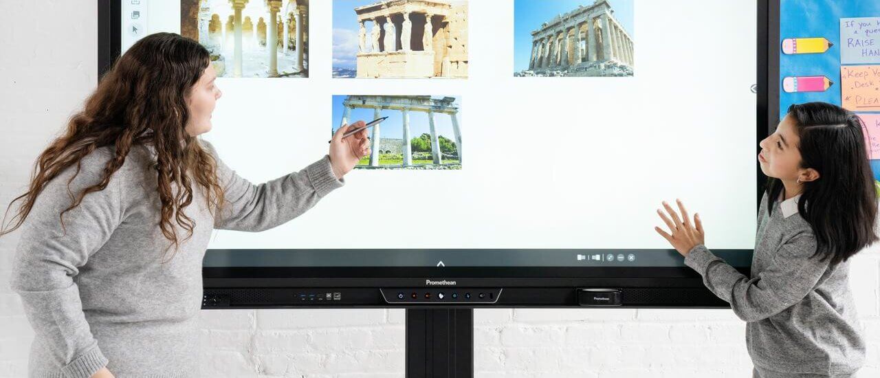 Deux étudiantes utilisent un écran numérique interactif pendant un exposé en classe sur l’histoire.