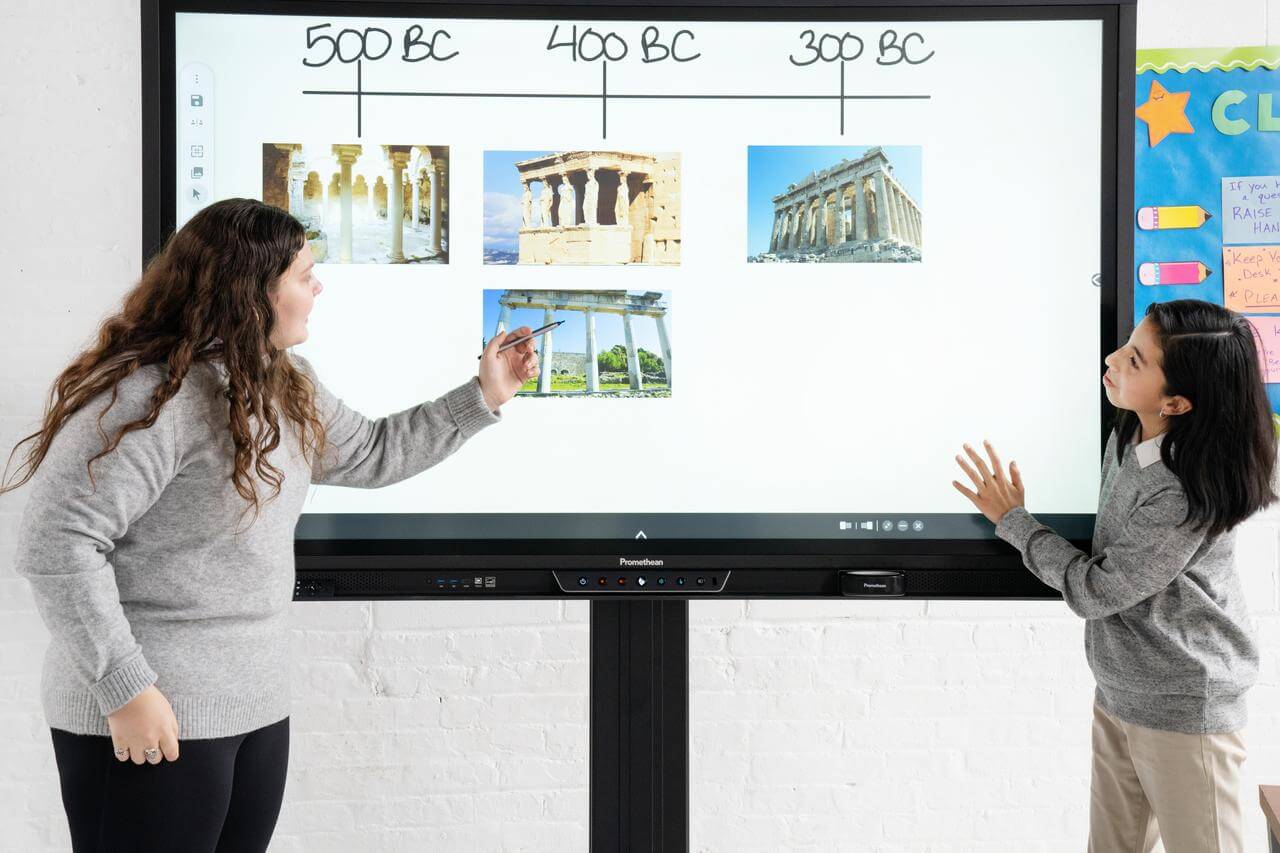 Deux étudiantes utilisent un écran numérique interactif pendant un exposé en classe sur l’histoire.